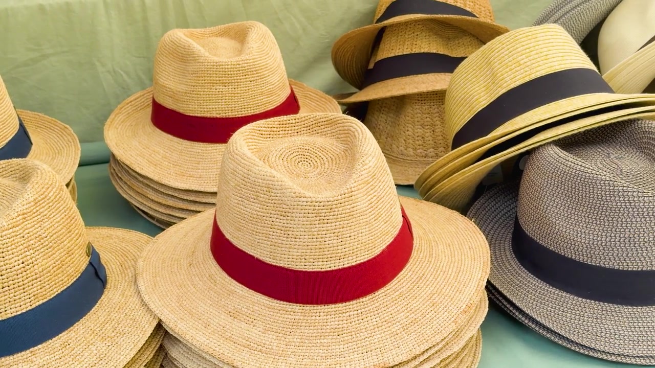 Una lenta panoramica su file di cappelli fedora di paglia fatti a mano in un mercato all'aperto.