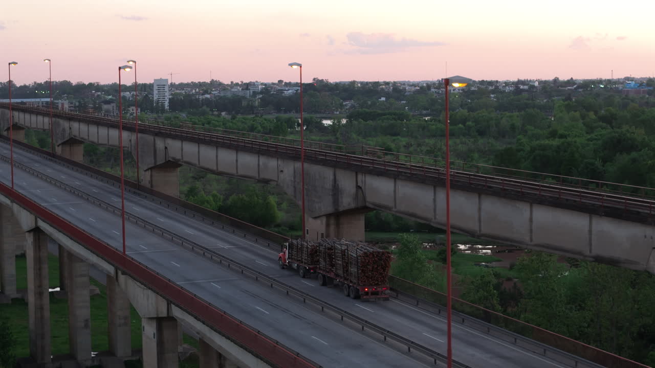 Truck loaded with tree trunks passes over bridge in urban area, industrial logging
