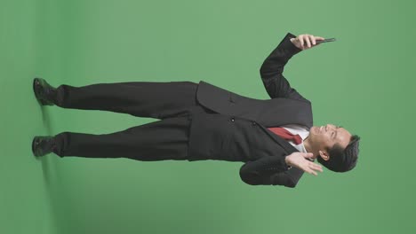 스튜디오에서 녹색 화면 배경에서 스마트 폰을 통해 누군가와 비디오 컨퍼런스 통화를 하는 아시아 사업가의 몸이 가득 차 있습니다.
