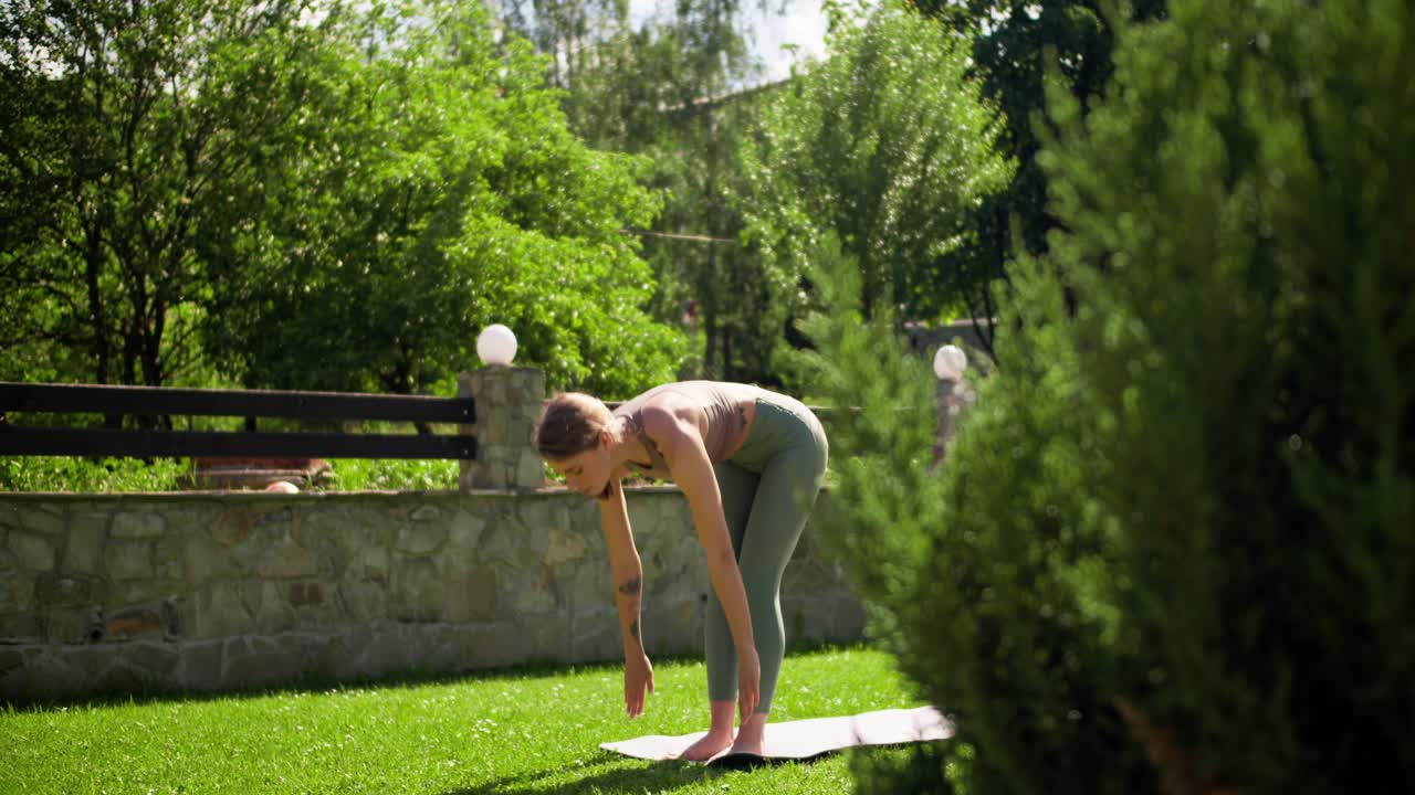 una chica rubia con ropa especial de verano hace yoga en una alfombra gris en un césped verde en verano. actividades deportivas en la naturaleza