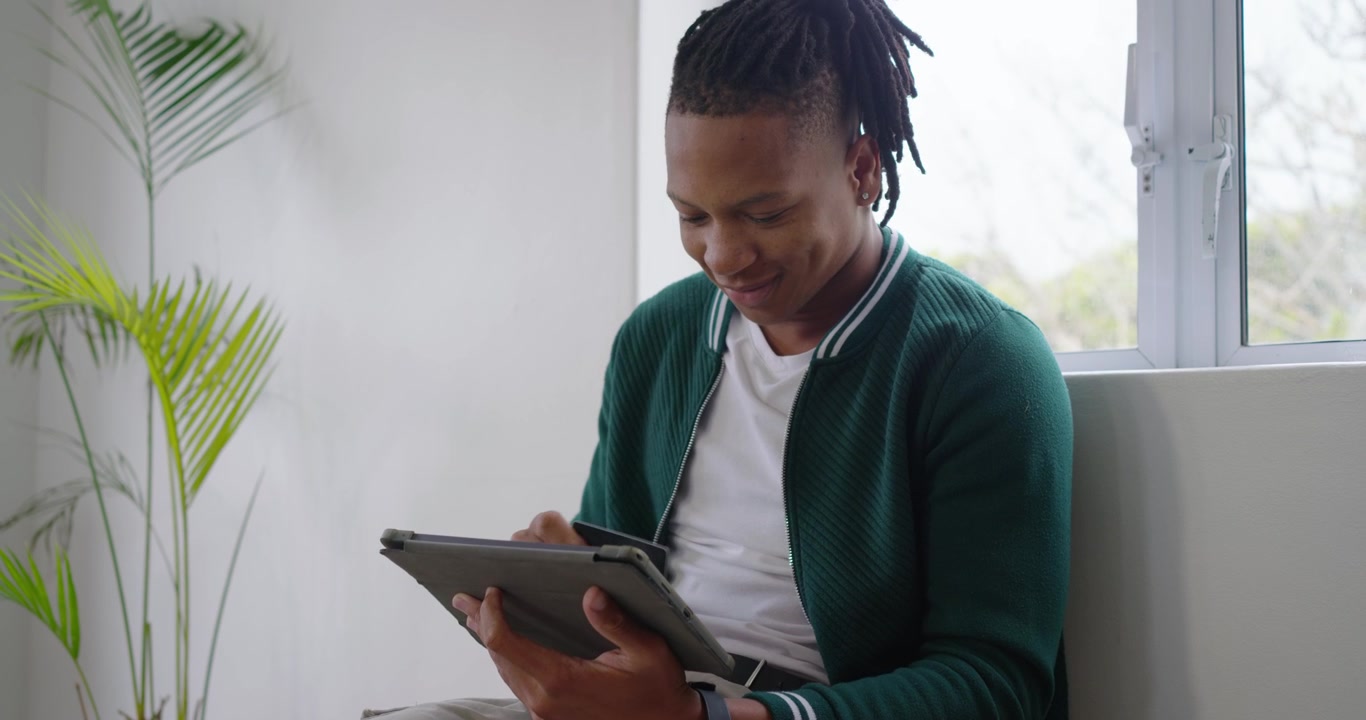 African American man sliding card into tablet folio, tapping screen to view content near window