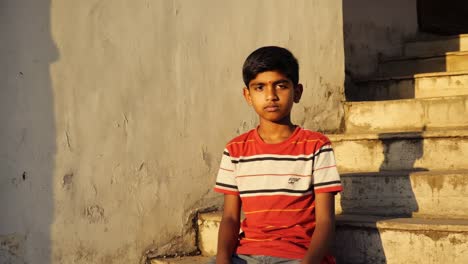young boy sits on concrete stairs, bathed in the warm glow of the golden hour, his contemplative expression adding a touch of quietude to the scene