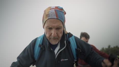 Two-hikers-with-backpacks-and-hiking-poles-walking-up-a-hill-to-rech-top-of-the-mountain-Stol