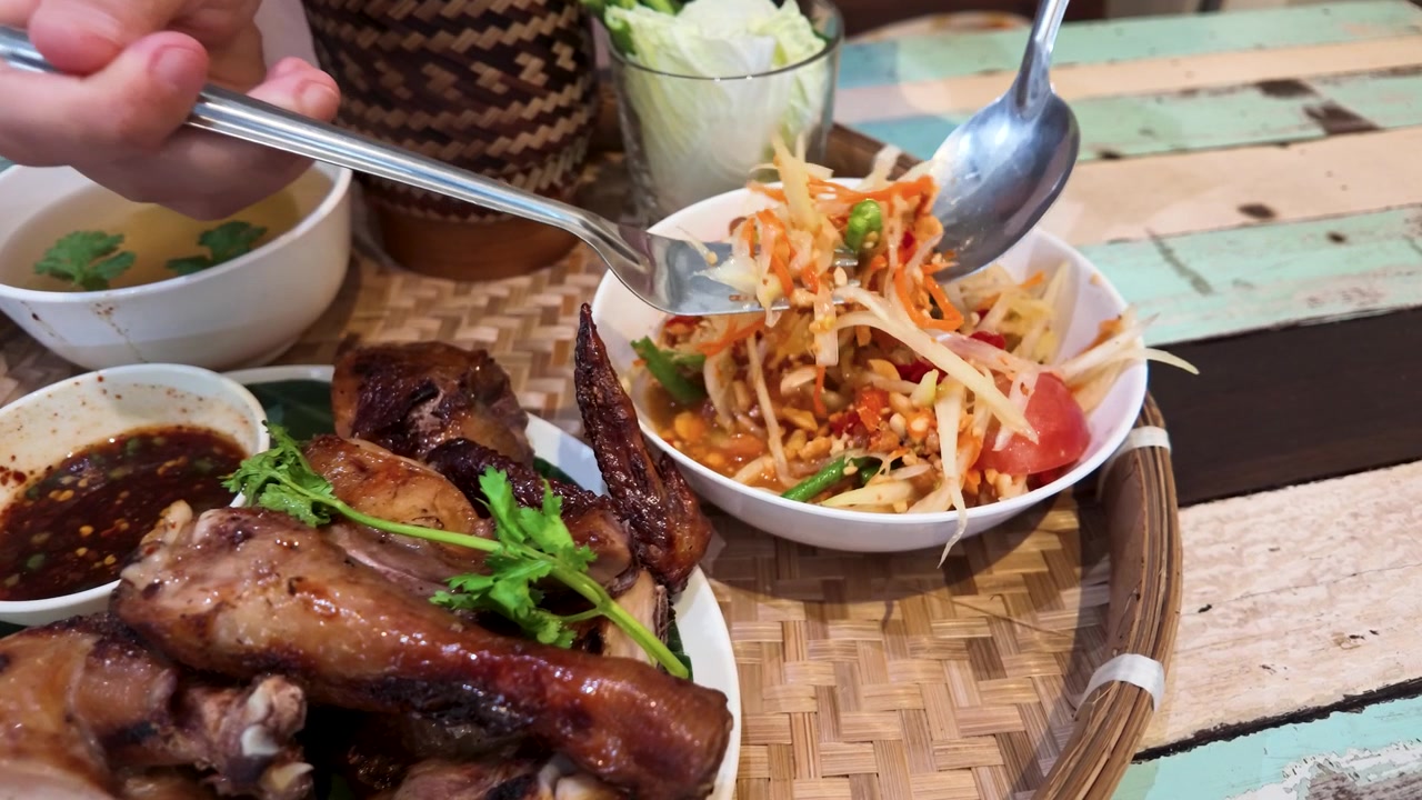 Close-up tangan sedang mengaduk salad pepaya pedas yang disajikan dengan ayam bakar di Bangkok, Thailand