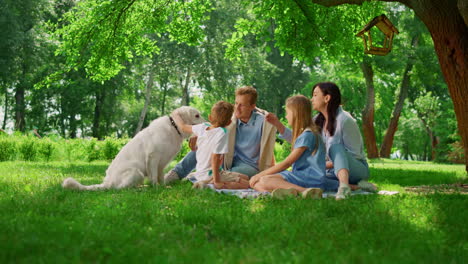 La-Joven-Familia-Acaricia-Al-Labrador-En-Un-Picnic.-La-Gente-Feliz-Descansa-Con-El-Perro-Afuera.