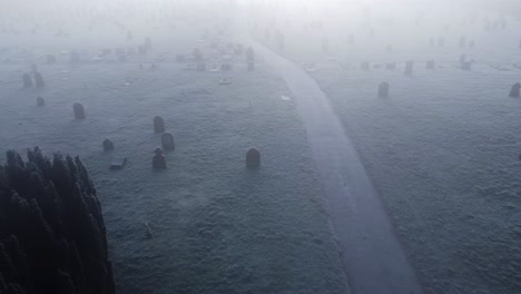 aerial drone shot over a foggy frozen thetford cemetery on london road showing snow filled grave yard on both sides of a path