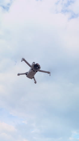 vertical clip of a mini drone hovering steadily in place beneath a partly cloudy sky. clear details of drone structure and calm weather conditions