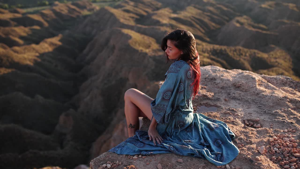 Woman sitting on a cliff overlooking a mountainous landscape