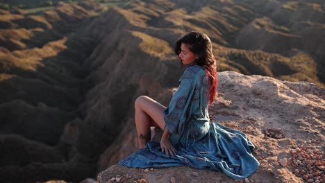 woman sitting on a cliff overlooking a mountainous landscape