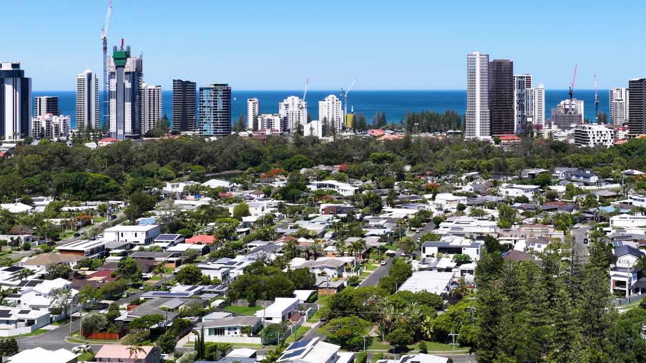 Daytime drone ascends from canal homes to reveal Gold Coast skyline, ocean, and urban landscape