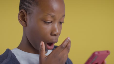 studio portrait of shocked boy on asd spectrum looking at mobile phone on yellow background