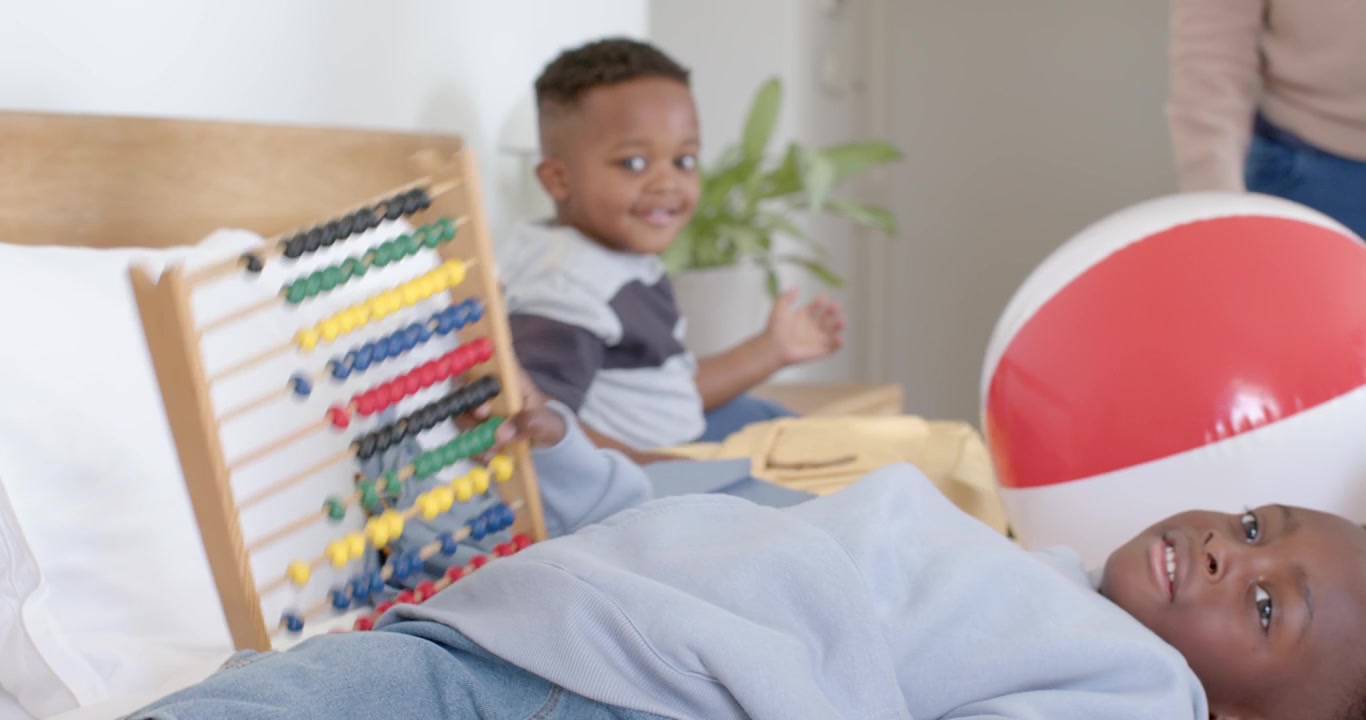 African American family watching boy exploring abacus for counting on bed while beach ball rolling