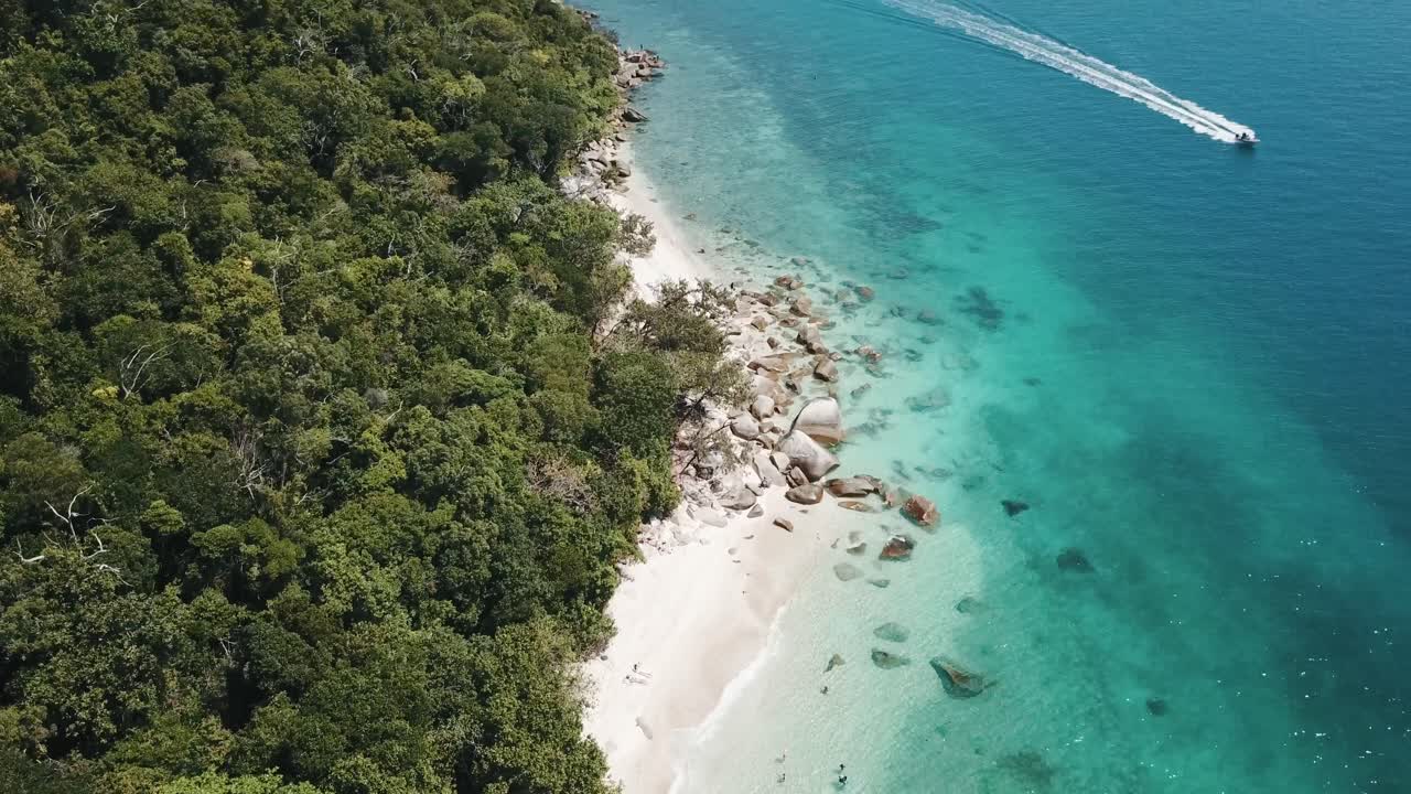 Drone aerial over tropical blue clear water and white sandy beach with a foresty island with a speed boat