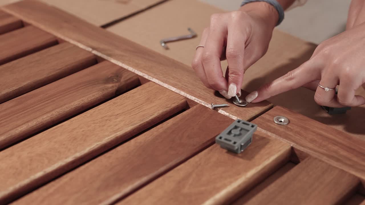 Hands assembling wooden furniture with screws and brackets in a well-lit indoor setting