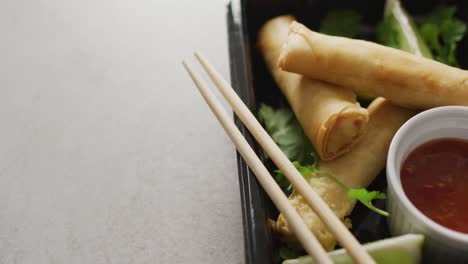 composition of plate with spring rolls and chilli sauce with chopsticks on grey background