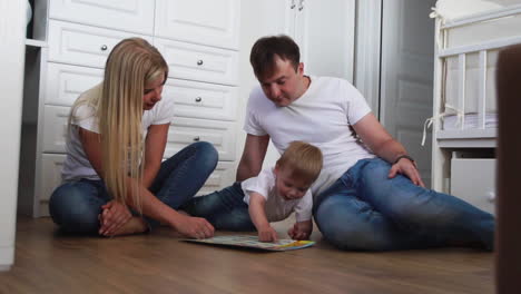 a family of three in white t-shirts and blue jeans sitting on the floor of their bedroom playing with the boy in intellectual games. slow-motion shooting happy family