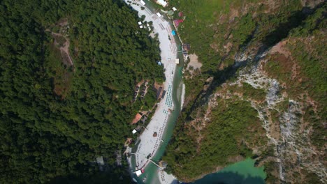 tourists sunbathing on emerald mountain river beach winding through alpine valley in shala, albania’s scenic wilderness