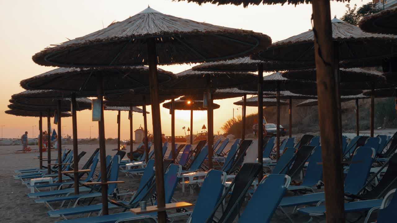 Beach with straw umbrellas and deck chairs at sunset, Greece
