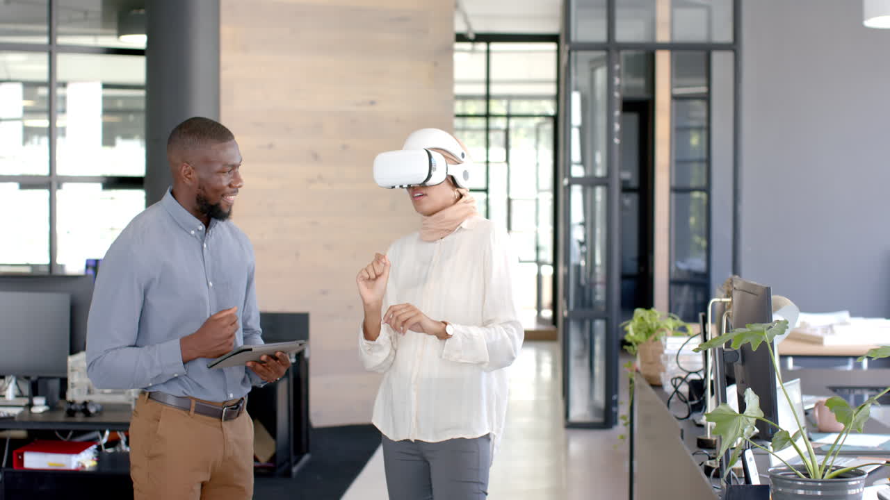 Using VR headset, woman discussing project with colleague holding tablet in office