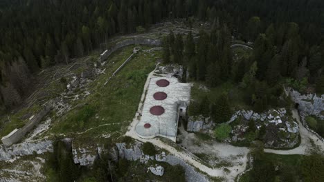 aerial drone orbits the historic forte campolongo, a world war i fortress on the asiago plateau. shows concrete gun emplacements and surrounding alpine forest, vicenza, italy