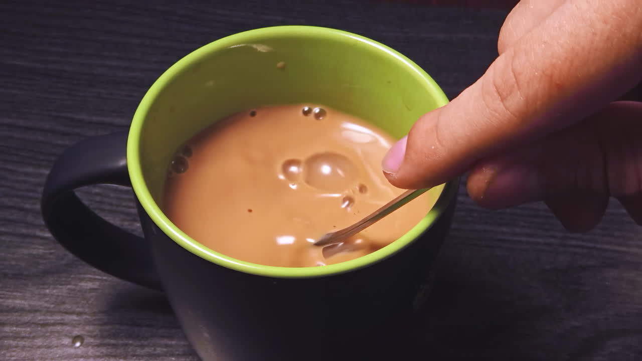 Primo piano al rallentatore di un uomo che mescola caffè nero con latte su un tavolo di legno in cucina