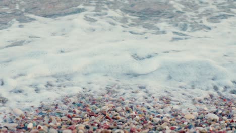 stunning 4k video of a rocky beach with foamy blue waves and multiple colour stones