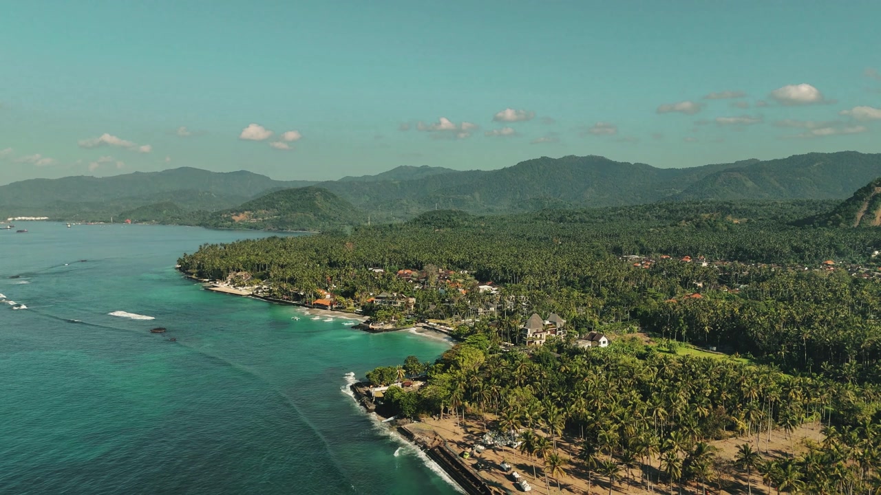 Aerial establishing pullback of Candi Dasa coastline in Bali with turquoise waters and lush greenery