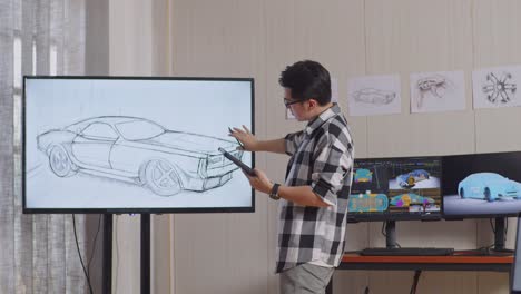 side view of asian male comparing his car design on a tablet to the photo on tv while working in the studio with computers display 3d electric car model