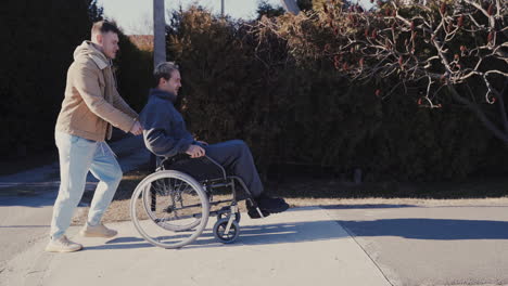 Young-Man-Running-While-Pushing-His-Disabled-Friend-In-Wheelchair-And-Having-Fun-Together