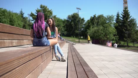 dos amigas atractivas hablando entre sí teniendo un buen estado de ánimo sentadas en un banco en el parque