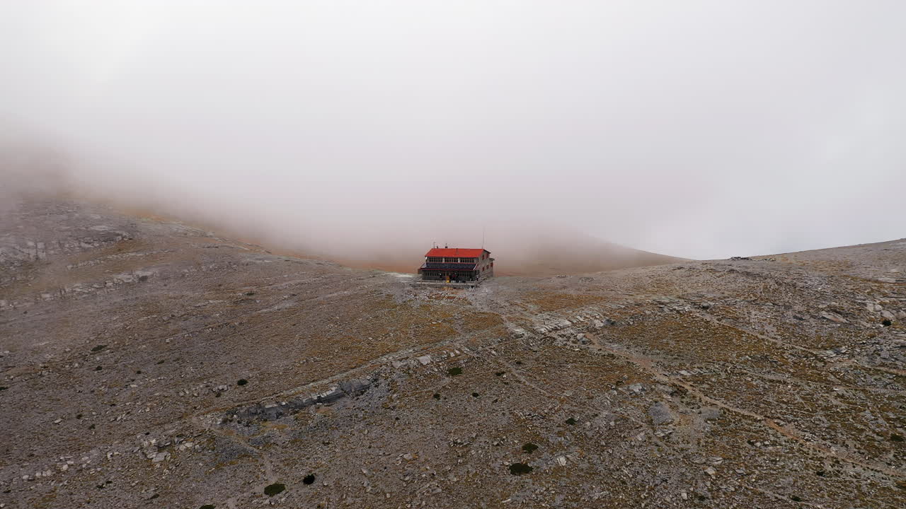 Langsom panorering med drone av Giosos Apostolidis tilfluktssted omgitt av vintertåke høyt oppe på Olymposfjellet, Hellas.