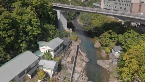 Aerial-rising-and-tilt-reveal-shot-revealing-beautiful-mountainous-scenery,-bridge-and-hotel-in-Jozankei-famous-hot-spring-onsen-town-in-Hokkaido,-Japan