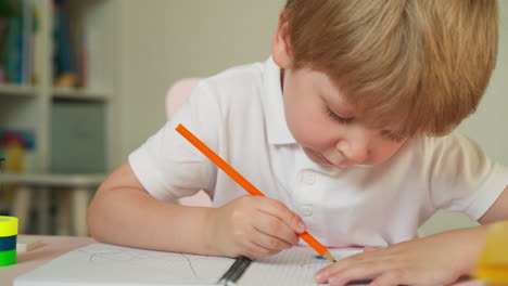 Toddler-examines-pencil-and-draws-picture-sitting-at-table