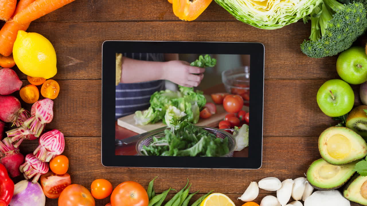 tableta con mujer haciendo ensalada y verduras en fondo de madera