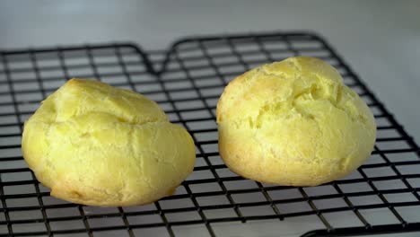 Hand-places-fresh-baked-choux-buns-on-cooling-rack,-close-up-cream-puff-pastry