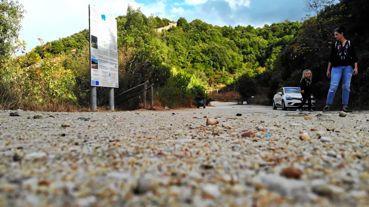 GREECE, ASPROVALTA - SEPTEMBER 26, 2020: A couple with a kid going up the wooden stairs to the unpaved road with a parked car. Greenery around