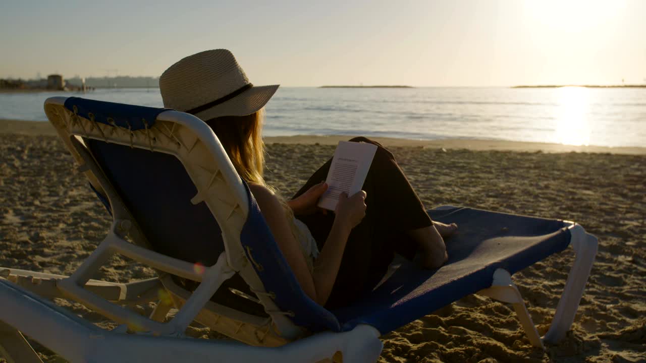 joven atractiva sentada en una hermosa playa leyendo un libro