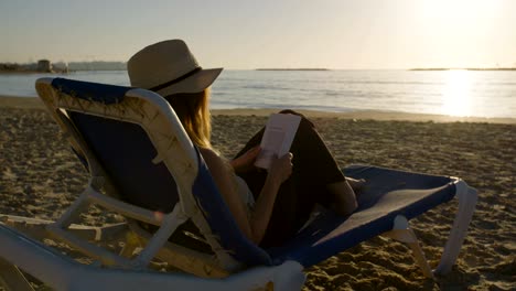 young attractive woman sitting on a beautiful beach reading a book