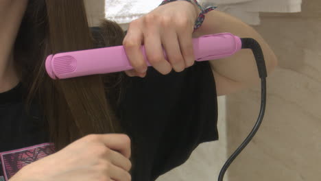 woman straightening her hair with a pink hair straightener in a bathroom