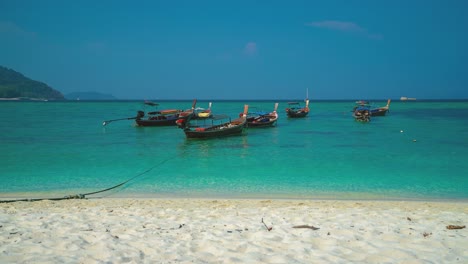 beautiful cinemagraph seamless video loop of traditional longtail boats at remote tropic asian seaside sand beach at perhentian island, malaysia with vibrant panoramic sea view. blue sky and turquoise water at scenic tourist vacation location