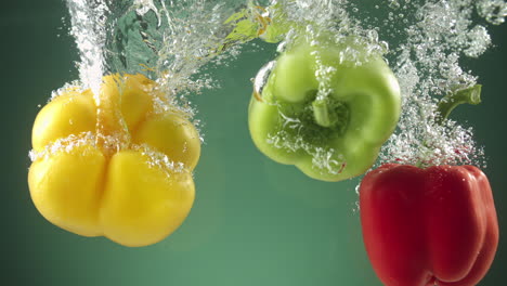 slow motion of colorful peppers falling into water on green background