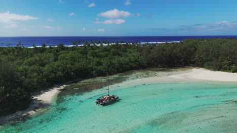catamarán de estacionamiento en la laguna turquesa de rarotonga, islas cook. vuelo aéreo subiendo de arriba hacia abajo. isla tropical con playa de arena y arrecife de coral. islas cook, nueva zelanda en verano. toma amplia.
