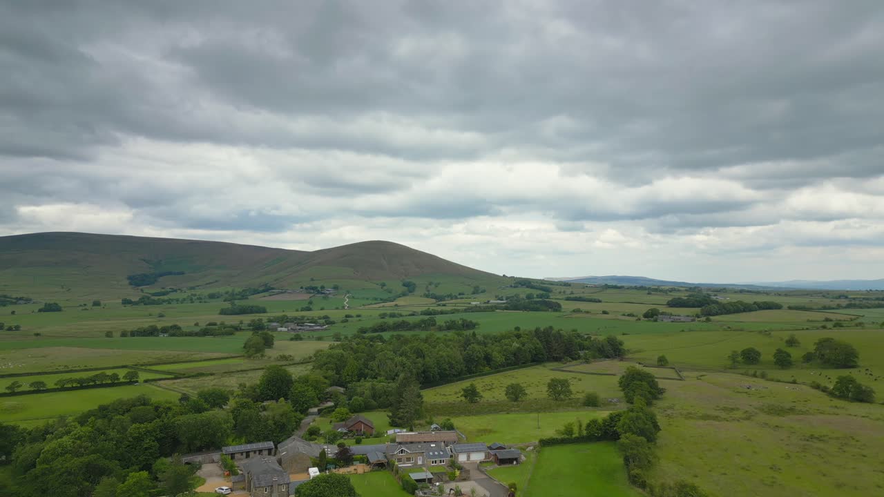 Campagna inglese in estate con sorvolo di una fattoria verso colline distanti in una giornata nuvolosa