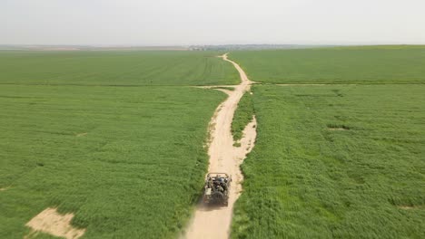 israel army golani infantry squad soldiers on humvee vehicle driving through green field at training ground country road - aerial tracking from behind