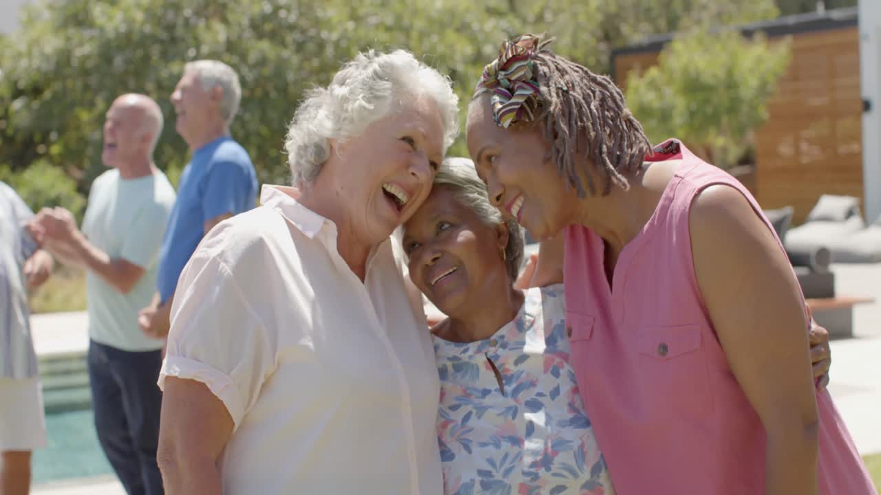 Happy diverse senior female friends embracing at sunny garden party, unaltered, in slow motion