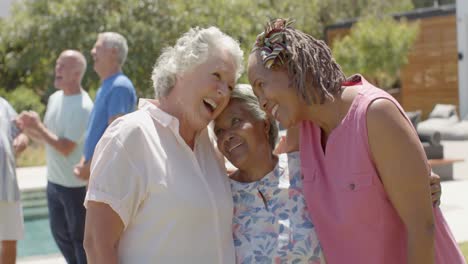 felices amigas mayores diversas abrazándose en una fiesta de jardín soleada, sin alteraciones, en cámara lenta