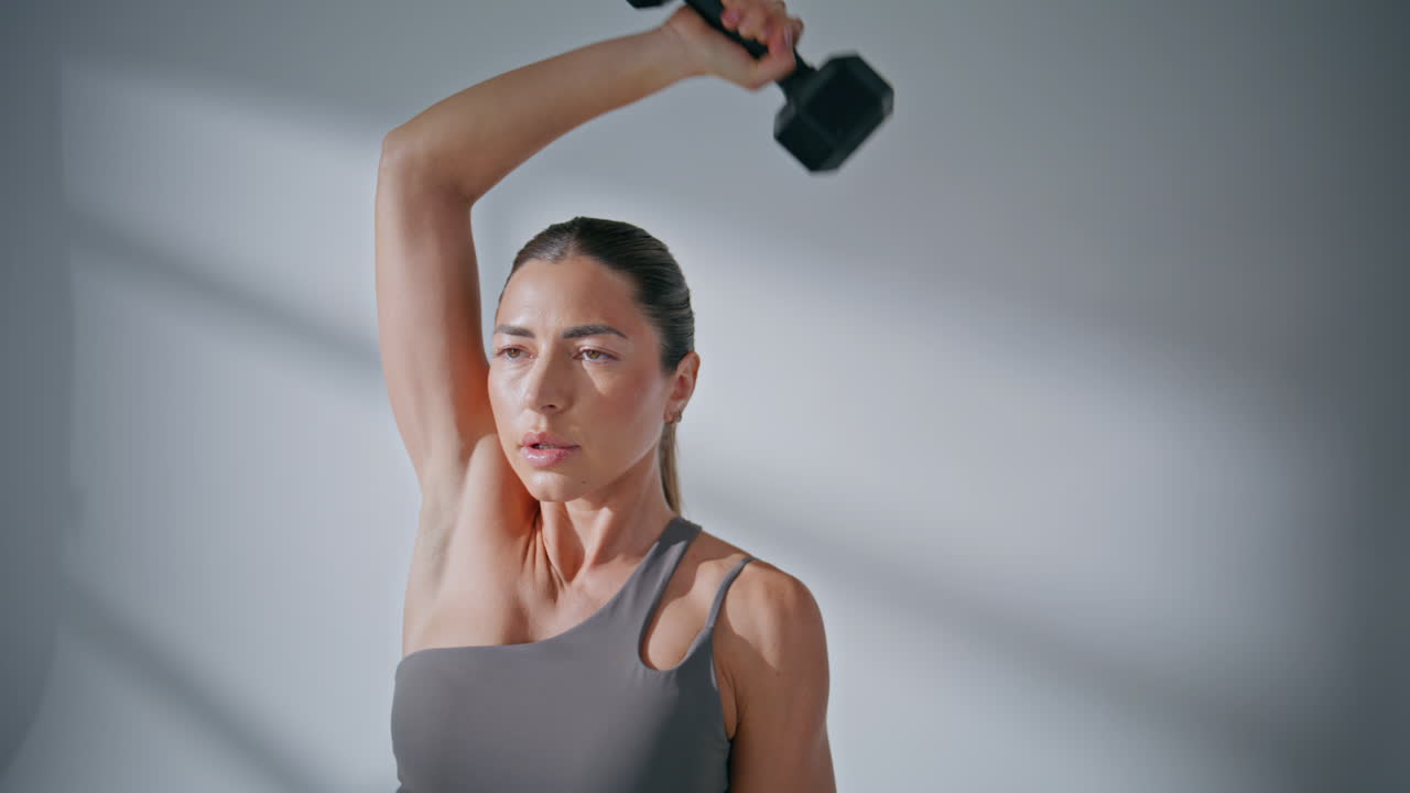 Strong woman lifting dumbbell pumping biceps at studio closeup. Lady workout