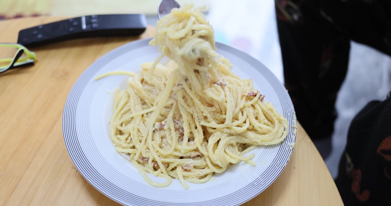 Uomo affamato avvolge con cura la carbonara cremosa attorno a una forchetta d'argento.