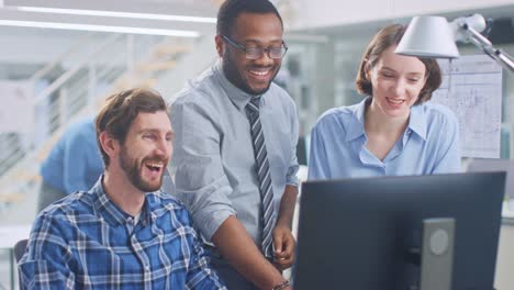 in the industrial engineering facility: male engineer working on desktop computer, female chief engineer and project manager discuss and explain to him project details. they smile, joke and cheer