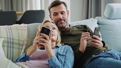 mature couple using a phone and lying on sofa